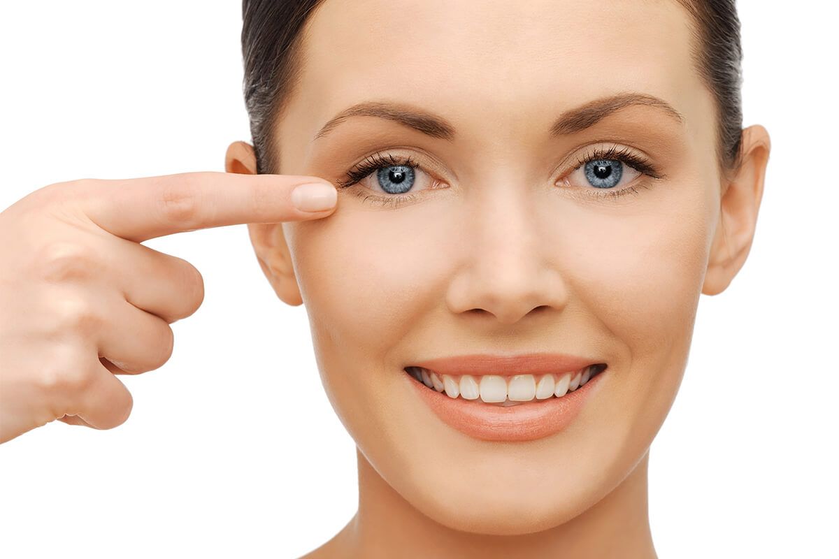 Woman pointing at her eye, smiling brightly.